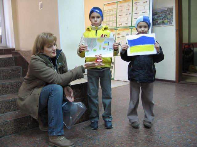 Альона Каїрцева приймає передачу від двох братиків, які принесли свою скарбничку і малюнки для бійців